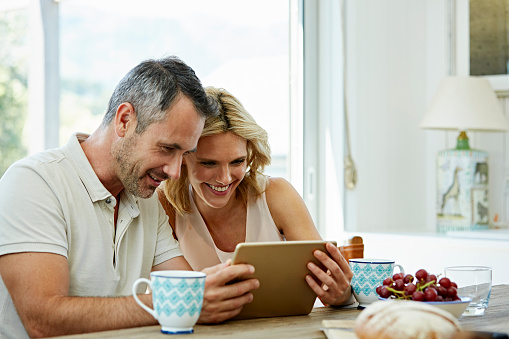 Happy couple using digital tablet at table in house