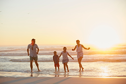 Happy family of four running on shore during sunset