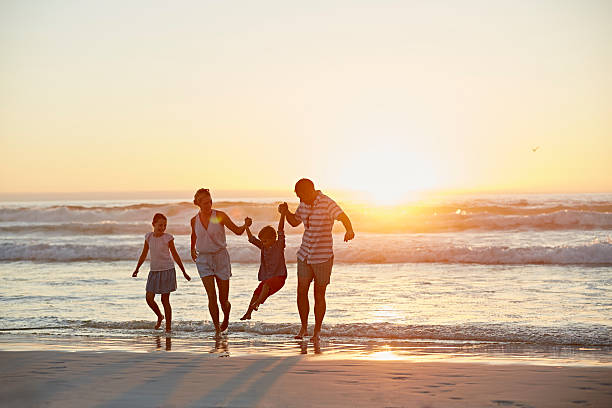 Parents with children enjoying vacation on beach Full length of parents with children enjoying vacation on beach during sunset walking in water stock pictures, royalty-free photos & images