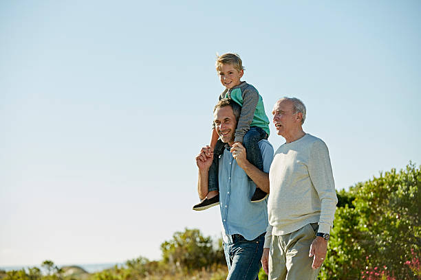 Happy three generation males walking on field Happy three generation males walking on field against clear sky multi generation family stock pictures, royalty-free photos & images