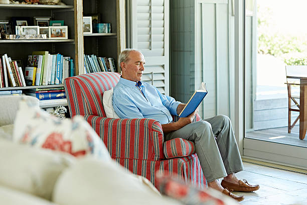 senior man reading book on chair - one person lifestyles 80 plus years indoors fotografías e imágenes de stock