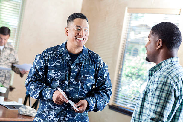 Mature soldier talking to young man at military recruitment event Mature adult Asian male soldier is smiling while working at military recruitment event. He is talking to young adult about joining the armed forces. us navy stock pictures, royalty-free photos & images