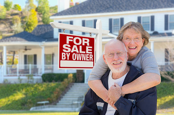 Senior Adult Couple in Front of Real Estate Sign, House Senior Adult Couple in Front of Home For Sale Real Estate Sign and Beautiful House. house for sale by owner stock pictures, royalty-free photos & images
