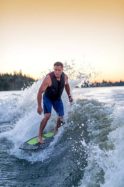 adult male wakesurfing a huge wake at sunset - waterskiing motorboating skiing water imagens e fotografias de stock