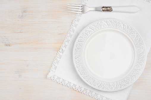 White ceramic plate with fork over placemat on wooden table