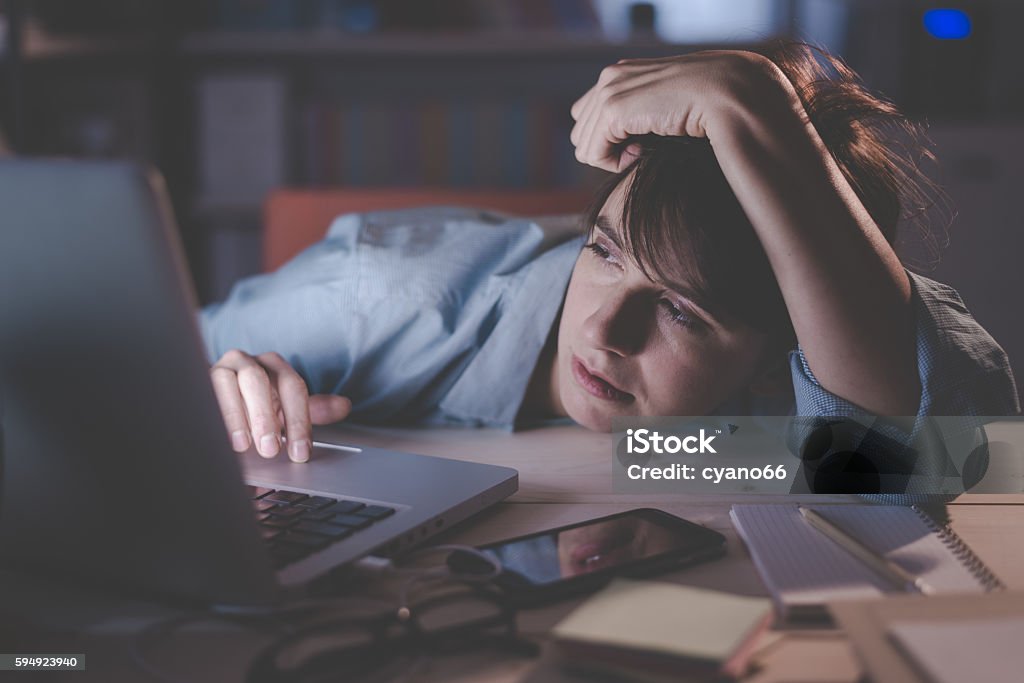Sleepy woman working with her laptop Sleepy exhausted woman working at office desk with her laptop, her eyes are closing and she is about to fall asleep, sleep deprivation and overtime working concept Adult Stock Photo