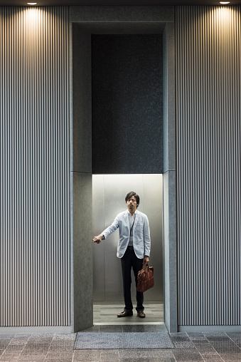 Japanese man wearing suit holding briefcase pressing button in elevator