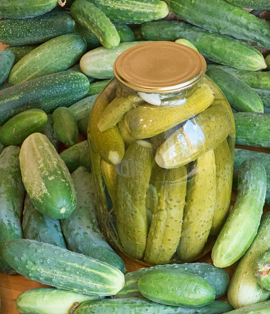 istock Big glass jar with pickles among fresh cucumbers. 594932588