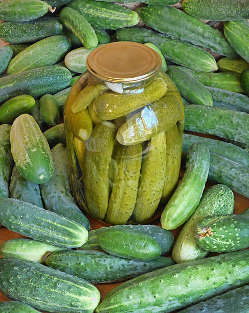 istock Big glass jar with pickles among fresh cucumbers. 594932714