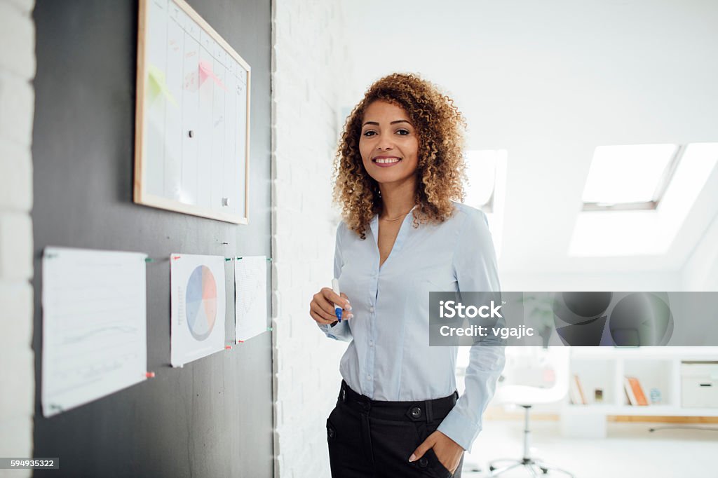 Latina Businesswoman Writing Schedule. Latina businesswoman standing near whiteboard and writing. She is making schedule for next business week. Looking at camera. One Woman Only Stock Photo