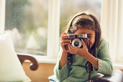 Shot of a little girl taking pictures with a vintage camera at home