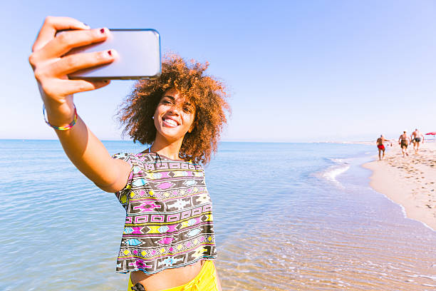 Young black woman taking a selfie at beach.  Twenty years old girl, mixed race caucasian and african black with curly hair. Travel and vacations concepts. Color filter added.