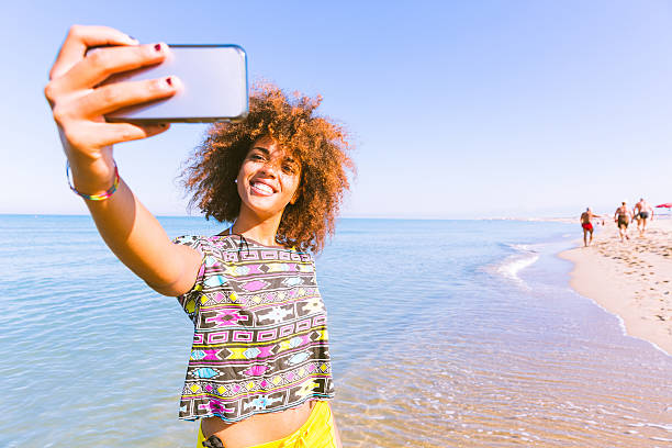 Young black woman taking a selfie at beach Young black woman taking a selfie at beach.  Twenty years old girl, mixed race caucasian and african black with curly hair. Travel and vacations concepts. Color filter added. selfie girl stock pictures, royalty-free photos & images