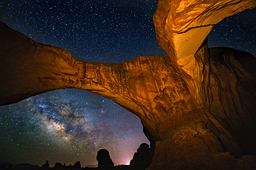 Iconic Balanced Rock and nearby sandstone rock formations silhouetted against the Milky Way in Arches National Park near Moab, Utah.