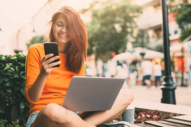 Woman texting outdoor Beautiful happy woman texting and using a laptop outside in the city. dyed red hair photos stock pictures, royalty-free photos & images