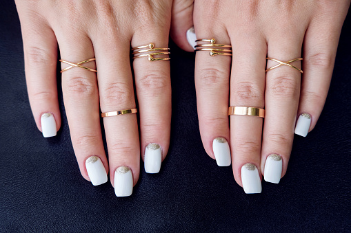 White nail art manicure, beauty hands with fashion gold rings. Trendy accessories top view
