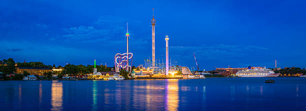Theme park fairground rides illuminated Tivoli Grona Lund Stockholm Sweden Stockholm, Sweden - July 7, 2016: Panoramic view across the blue waters of Riddarfjarden to the rollercoasters and fairground rides of Gruna Lund amusement park illuminated at night on Djurgarden in central Stockholm, Sweden's picturesque capital city. Composite panoramic image created from nine contemporaneous sequential photographs. djurgarden photos stock pictures, royalty-free photos & images