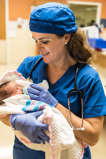 Caucasian female mature nurse feeding a newborn baby