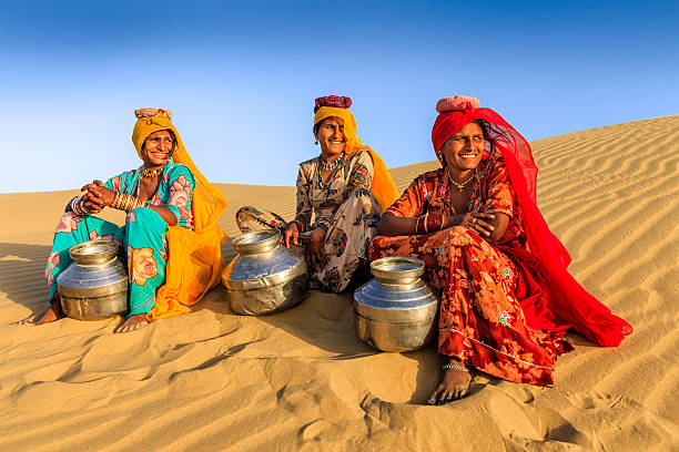 Indian women carrying water from local well, desert village, India Indian women crossing sand dunes and carrying on their heads water from local well, Thar Desert, Rajasthan, India. Rajasthani women and children often walk long distances through the desert to bring back jugs of water that they carry on their heads. Panoramic view. thar desert stock pictures, royalty-free photos & images
