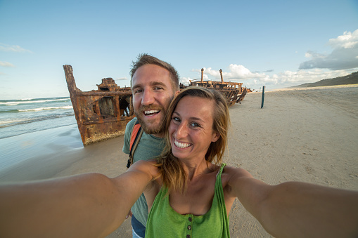Young couple traveling take a selfie portrait with the Iconic Maheno Shipwreck on Fraser Island, Queensland, Australia.