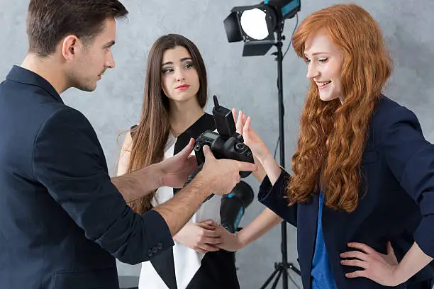 Young photographer talking to a designer with a criticising look on his face, next to a fussy model