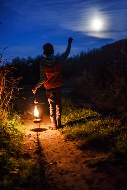 boy with an ancient candle lamp in hands outdoors child with a lantern waving a hand to someone in the dark lanterns at night stock pictures, royalty-free photos & images