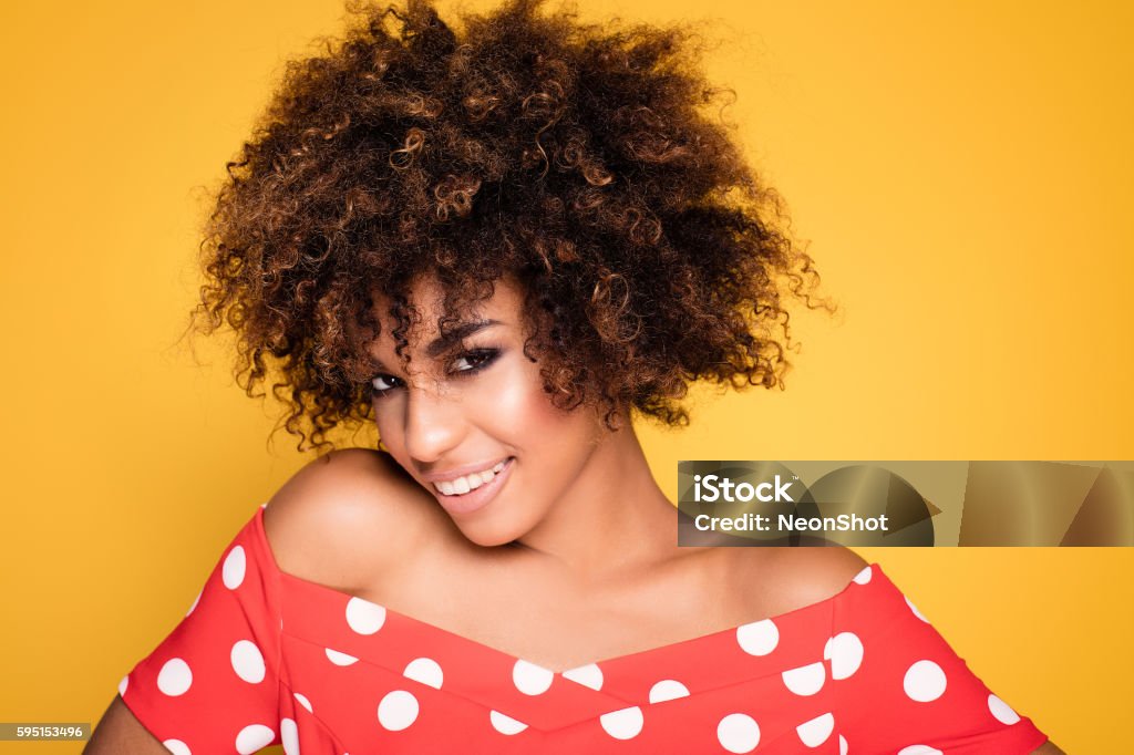 Beauty portrait of smiling girl with afro. Beauty portrait of young african american girl with afro hairstyle. Girl posing on yellow background, looking at camera, smiling. Studio shot. Adult Stock Photo