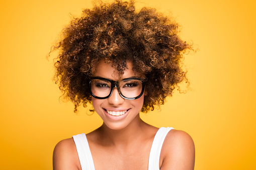 Young beautiful african american girl with an afro hairstyle. Laughing girl wearing eyeglasses. Portrait. Yellow background. Girl looking at camera.