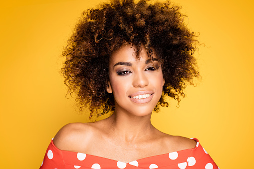 Beauty portrait of young african american girl with afro hairstyle. Girl posing on yellow background, looking at camera, smiling. Studio shot.
