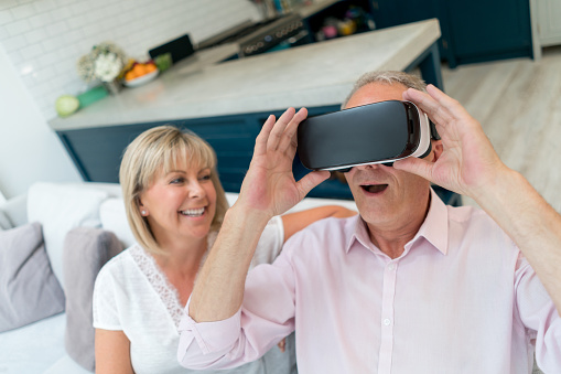 Portrait of a senior couple a home trying a VR device and looking very happy