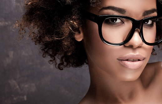 Portrait of young african american girl with afro, wearing fashionable eyeglasses, looking at camera. Studio shot.