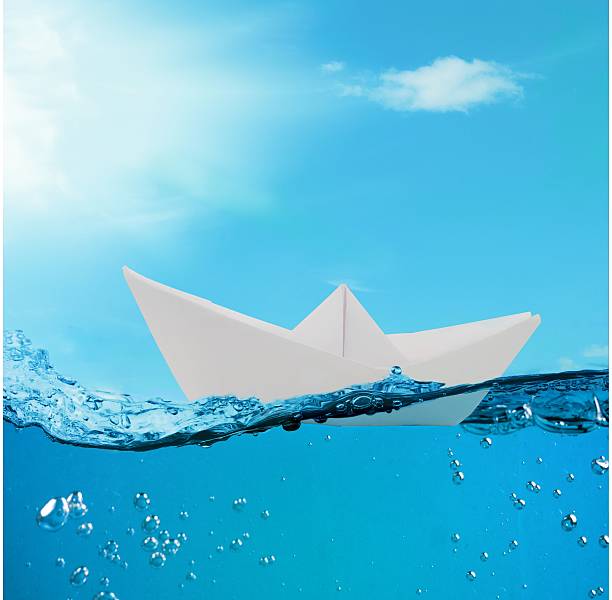 istock paper boat floating among the waves in the ocean 595323642