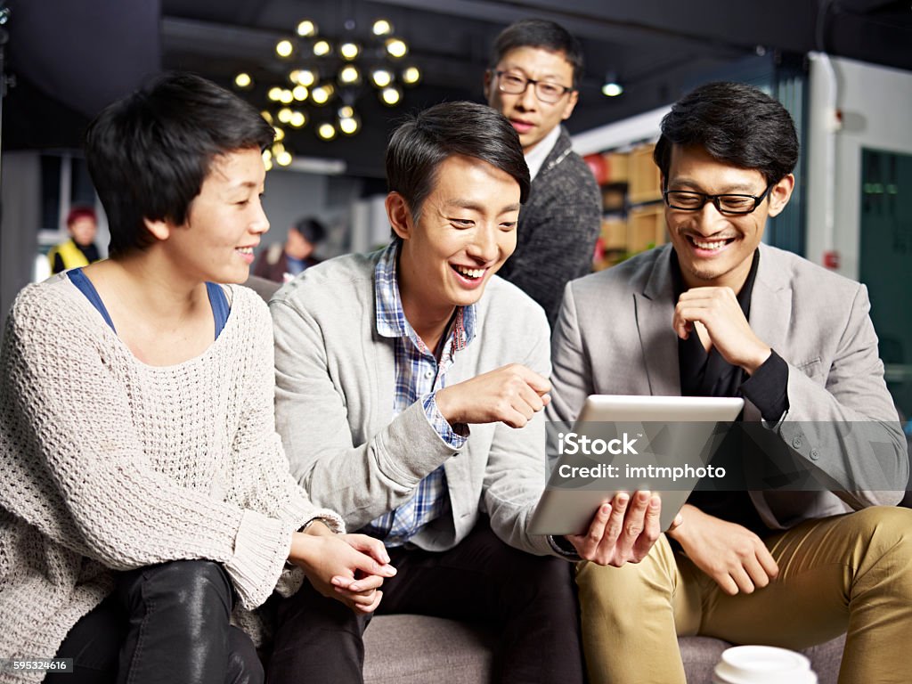 young asian business people using tablet in office young asian businesspeople sitting in sofa looking at tablet computer, happy and smiling. Asian and Indian Ethnicities Stock Photo