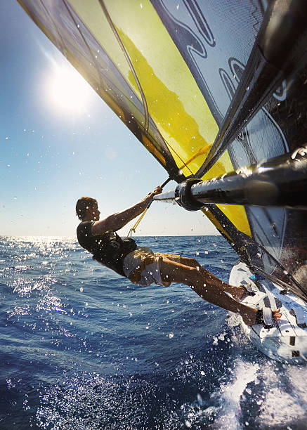 Windsurfing in sea with splashing water Windsurfing in sea with splashing water. Perspective from behind on sail towards the surfer. windsurfing stock pictures, royalty-free photos & images