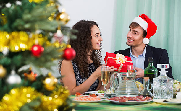 Happy man giving present to woman during Christmas dinner Happy man giving present to  woman during Christmas dinner in home wonderingly stock pictures, royalty-free photos & images