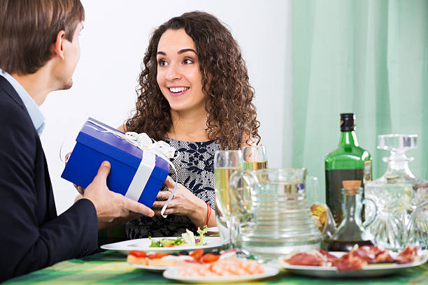 Man giving present to woman Man giving present to happy woman during romantic dinner in home wonderingly stock pictures, royalty-free photos & images