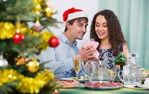 Man giving present to woman during Christmas dinner Man giving present to woman during Christmas dinner in home wonderingly stock pictures, royalty-free photos & images
