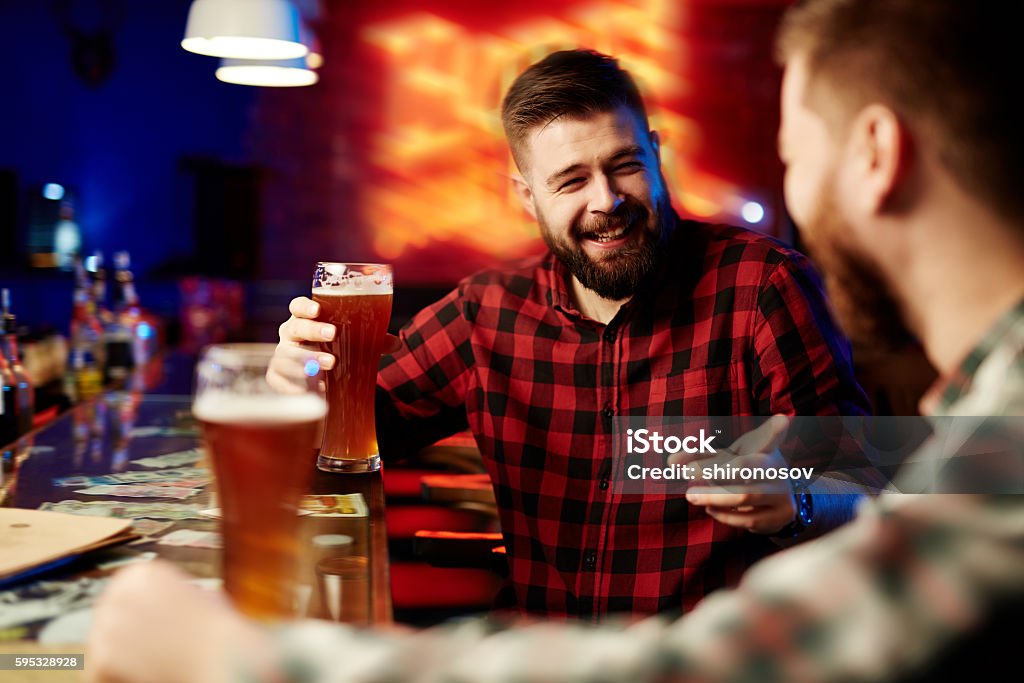 Drinking beer at bar Man drinking beer and laughing with his friend Drinking Stock Photo