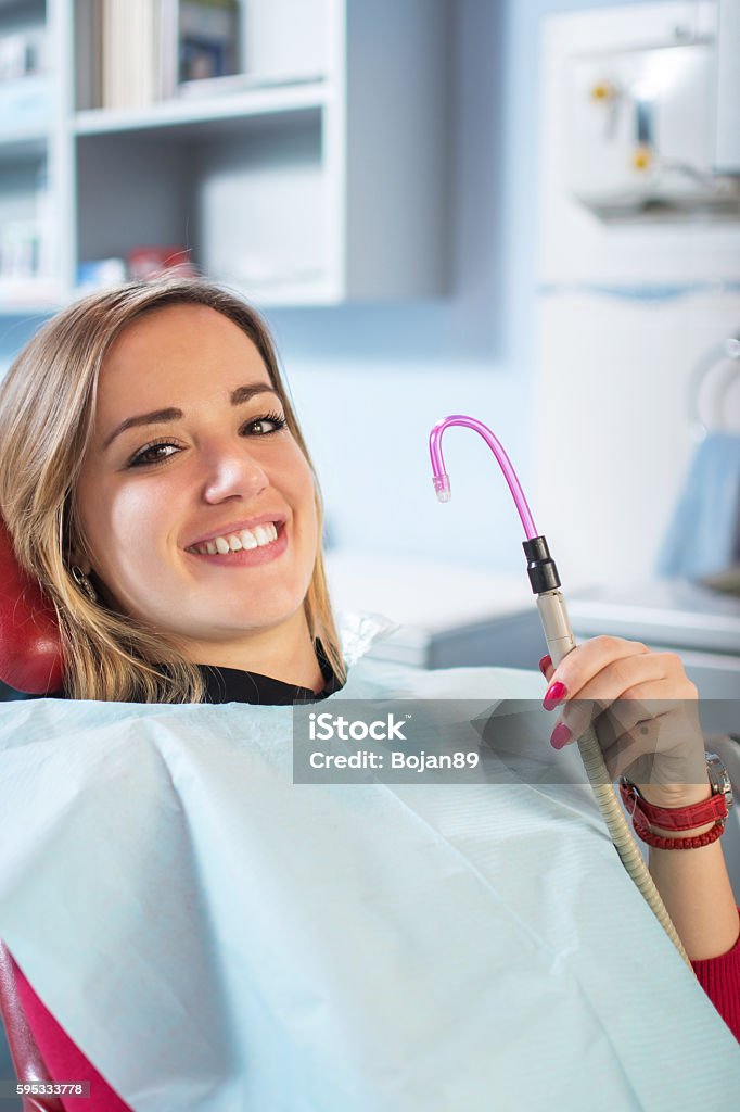 Young female patient smiling and holding suction tube. Dental Equipment Stock Photo