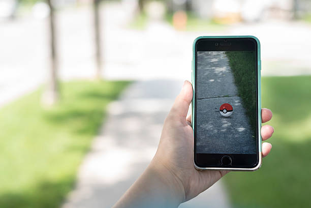 Moorhead, Minnesota, United States - July 23, 2016: Hand holding up screen of Pokemon GO gameplay while walking down suburban street. On the iPhone screen you can see a red Pokemon ball. 