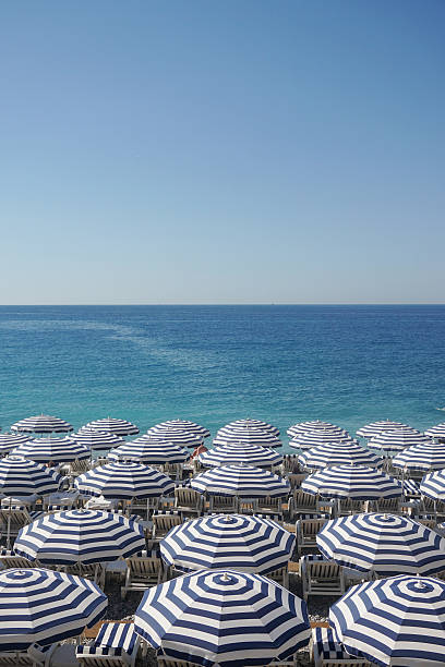 Beach umbrellas and sun loungers on a beach Rows of sun loungers and umbrellas on a beach with calm blue sea french riviera stock pictures, royalty-free photos & images