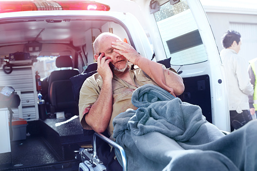 Hombre angustiado en camilla hablando por teléfono celular detrás de ambulancia photo