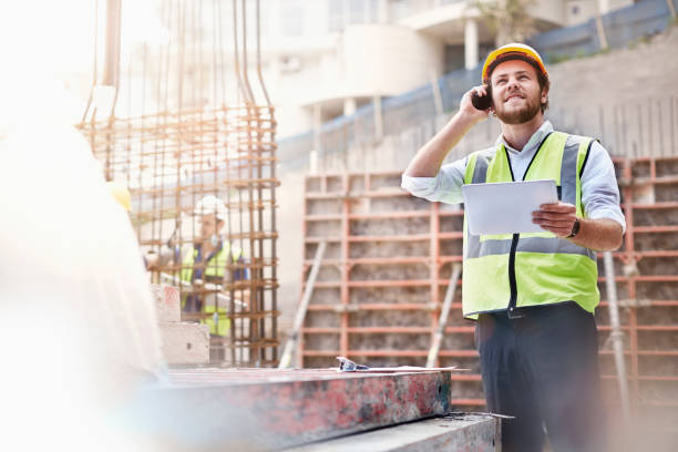Engineer with digital tablet talking on cell phone at construction site stock photo