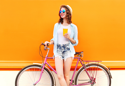 Fashion pretty woman with coffee or juice cup and retro vintage bicycle over colorful orange background