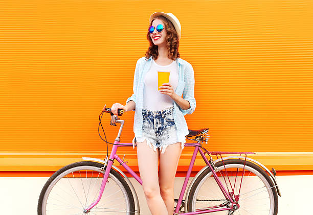 Fashion woman with coffee or juice cup and retro bicycle Fashion pretty woman with coffee or juice cup and retro vintage bicycle over colorful orange background juice drink stock pictures, royalty-free photos & images