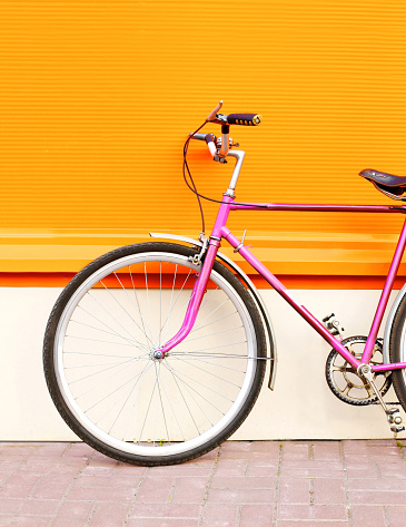 Retro pink bicycle stands over colorful orange background closeup