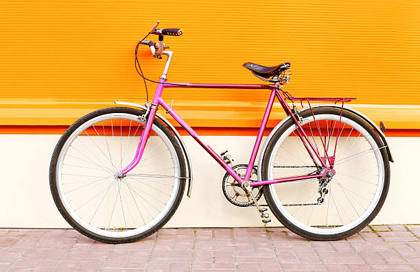 istock Retro pink bicycle stands over colorful orange background 595354754