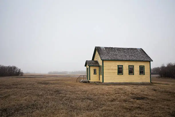An old repainted yellow with green trim abandoned schoolhouse in a foggy spring rural landscape