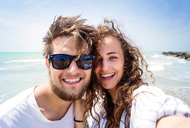 beau couple sur la plage, rire, prendre du selfie, sourire - face to face teenage couple teenager couple photos et images de collection