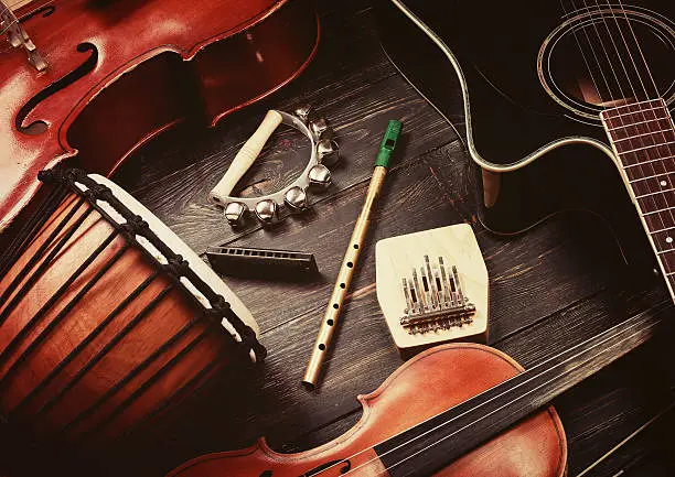 Set of musical instruments on dark wooden background: guitar, violin, harmonica, cello and others. Top view. Vintage retro effect filtered, hipster style